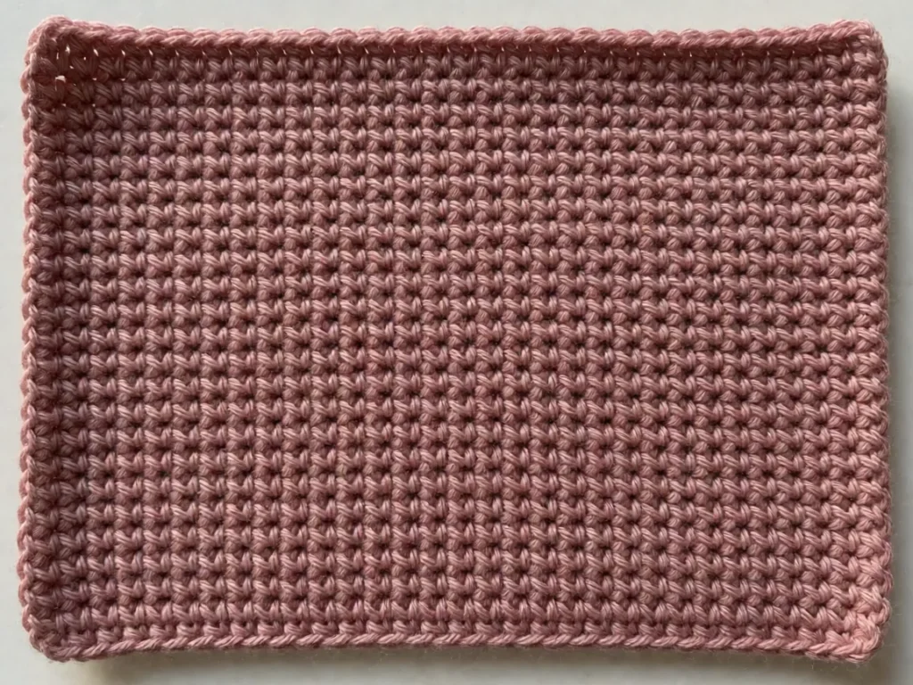 Flat single crochet fabric in dusty rose yarn showing the dense grid of small tight stitches it produces